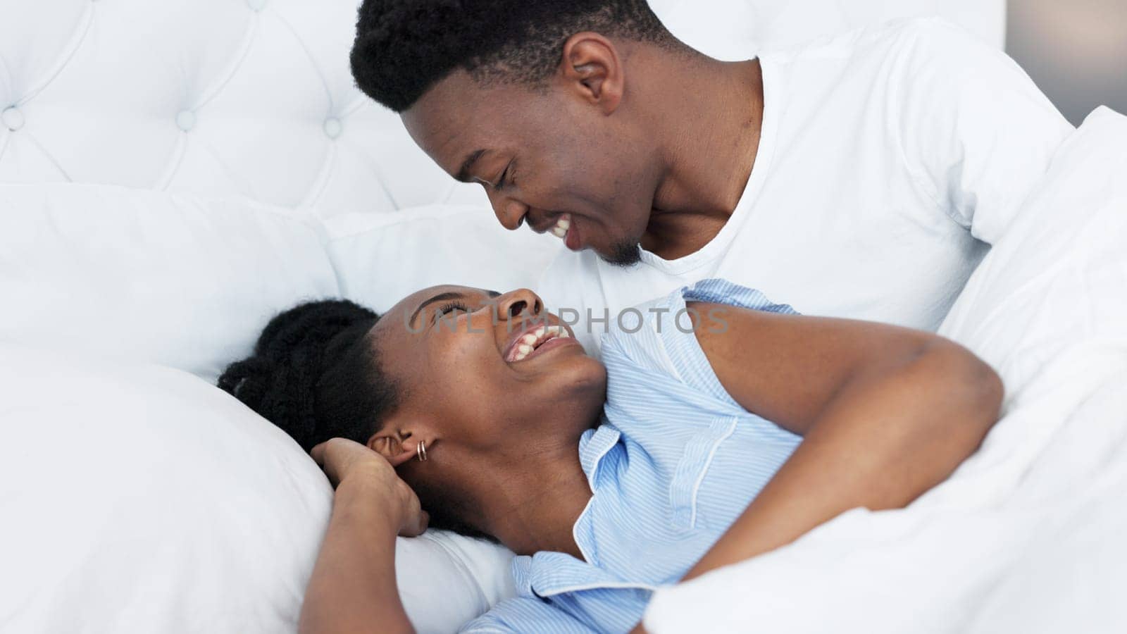 Happy black couple in bedroom kiss and smile for love, romance and intimacy at house or home in morning. Young, happiness and kissing black woman and man or romantic black people dating bond together by YuriArcurs