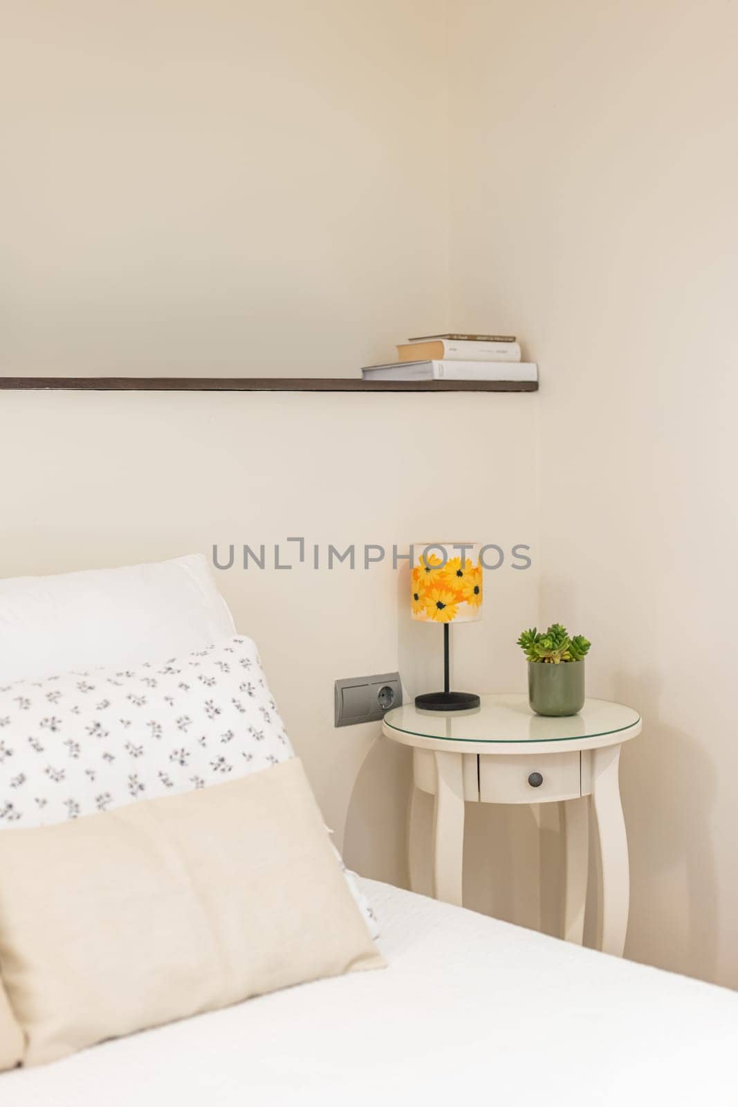 Close-up corner of cozy bedroom in light white colors with bedside table with lamp and shelf next to the bed with linen and a pillow. Concept of a calm and concise interior by apavlin