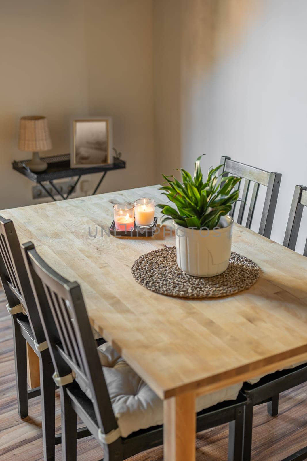 Top view of wooden dining table with chairs and decorative elements plant, candles, pillows on a light wall background. Concept of stylish interior and natural materials in the decor.