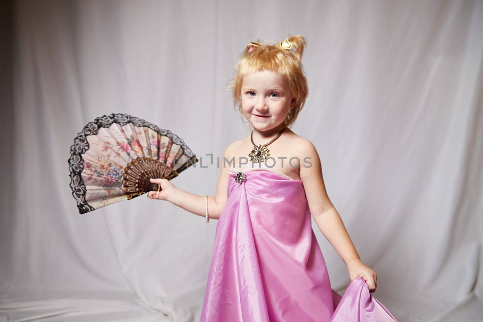 Portrait of cute kid girl posing in pink beautiful dress on white background. Young female model looking as magic princess from fairy taly