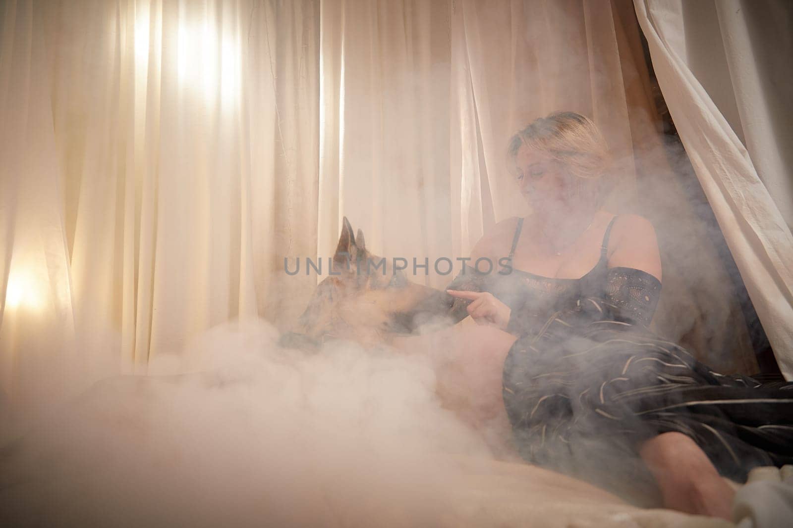 Portrait of sexual body positive adult lady woman in an intimate in tender space indoors in bedroom with big shepherd dog. Plump girl poses with pet in black underwear during boudoir style photo shoot by keleny