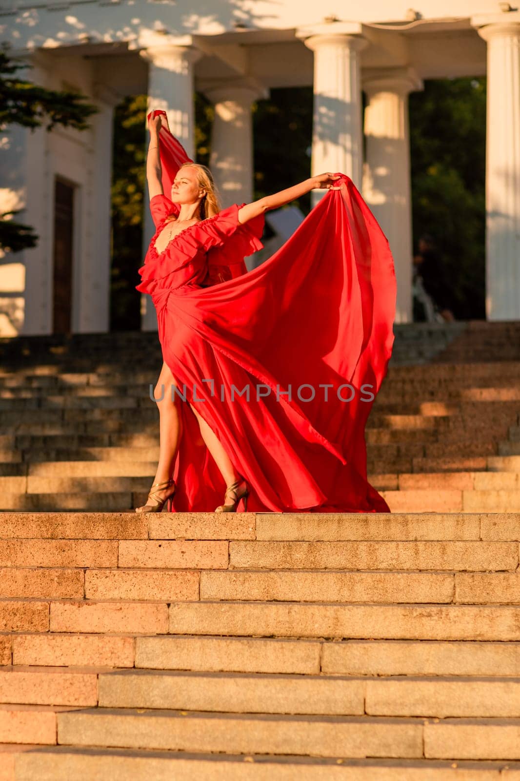 A woman in a long red dress against the backdrop of sunrise, bright golden light of the sun's rays. The concept of femininity, harmony. by Matiunina