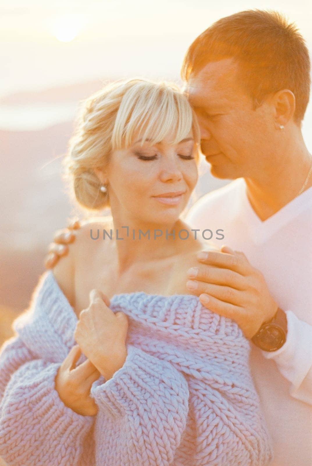Man hugs woman from behind by the shoulders, touching her temple with his face. High quality photo