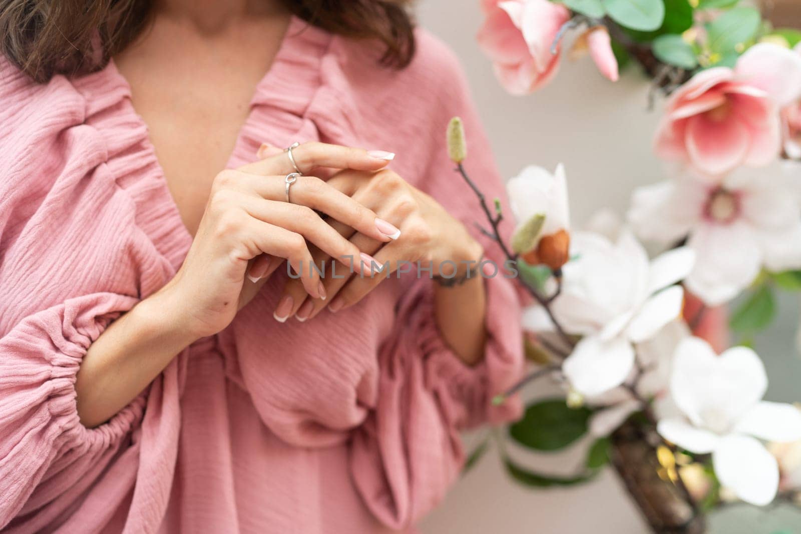 Close shot of romantic cute french gel polish manicure nails. Woman in pink summer dress with flowers around. Rings on fingers. Outdoor shot.