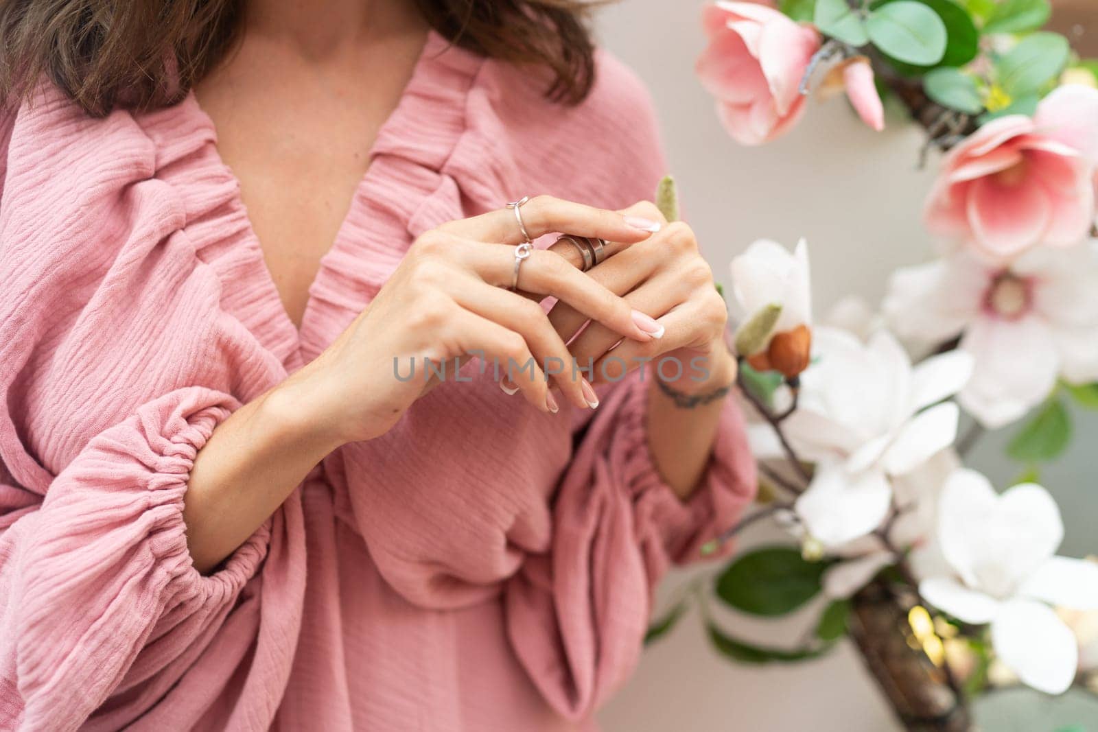 Close shot of romantic cute french gel polish manicure nails. Woman in pink summer dress with flowers around. Rings on fingers. Outdoor shot.