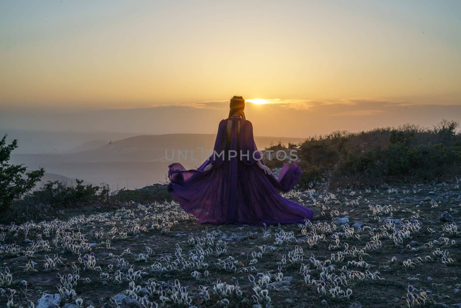 Sunset purple dress woman mountains. Rise of the mystic. sunset over the clouds with a girl in a long purple dress. In the meadow there is a grass dream with purple flowers. by Matiunina