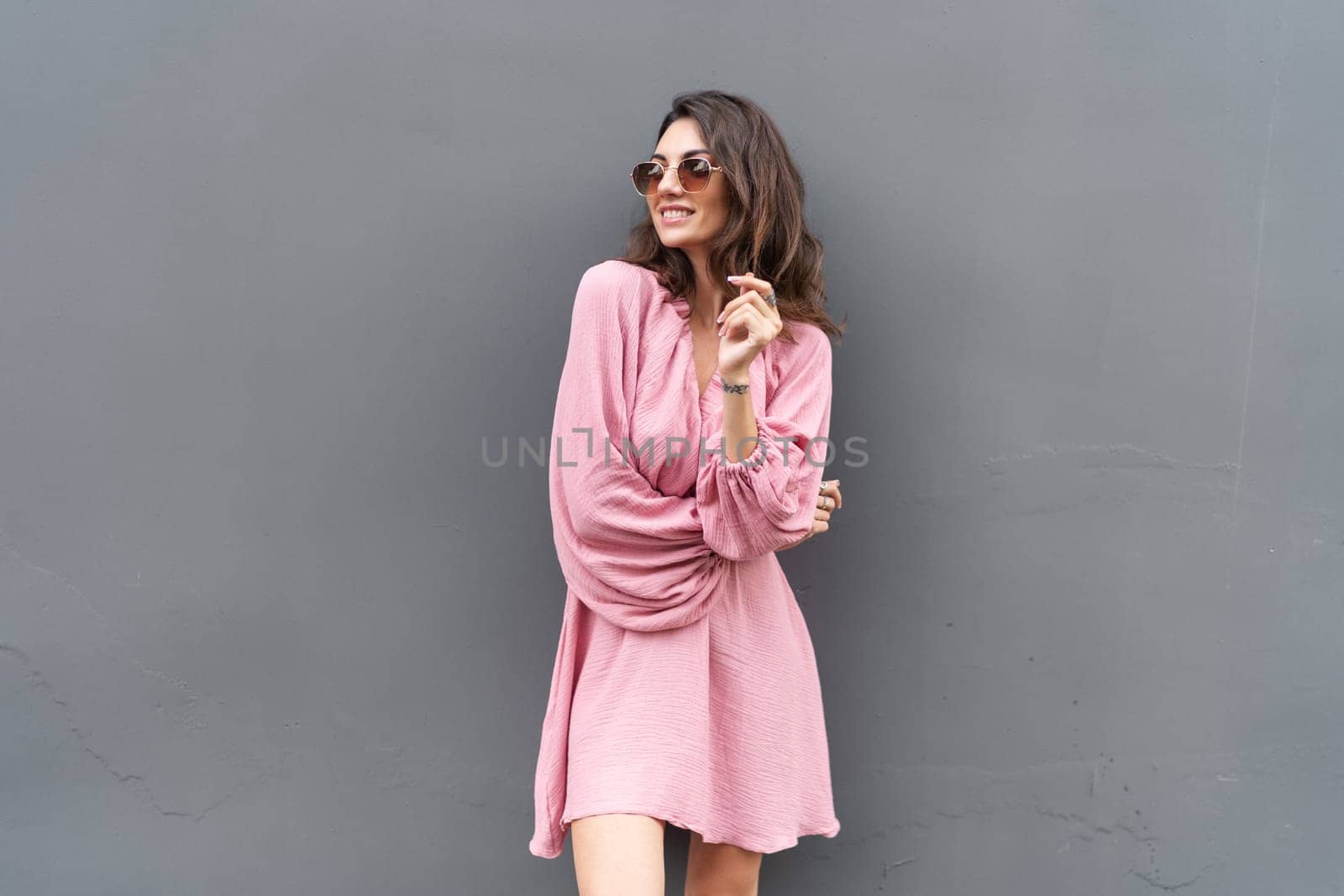 Young beautiful smiling cute romantic woman in trendy summer dress. Carefree woman posing in the street near grey wall. Positive model outdoors in sunglasses. Cheerful and happy.