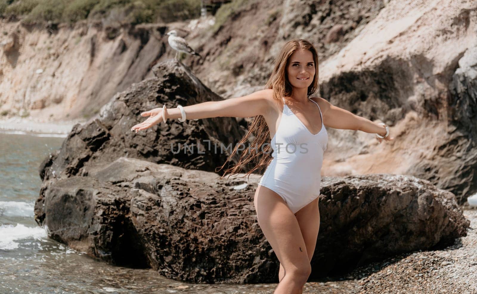 Woman travel sea. Young Happy woman in a long red dress posing on a beach near the sea on background of volcanic rocks, like in Iceland, sharing travel adventure journey