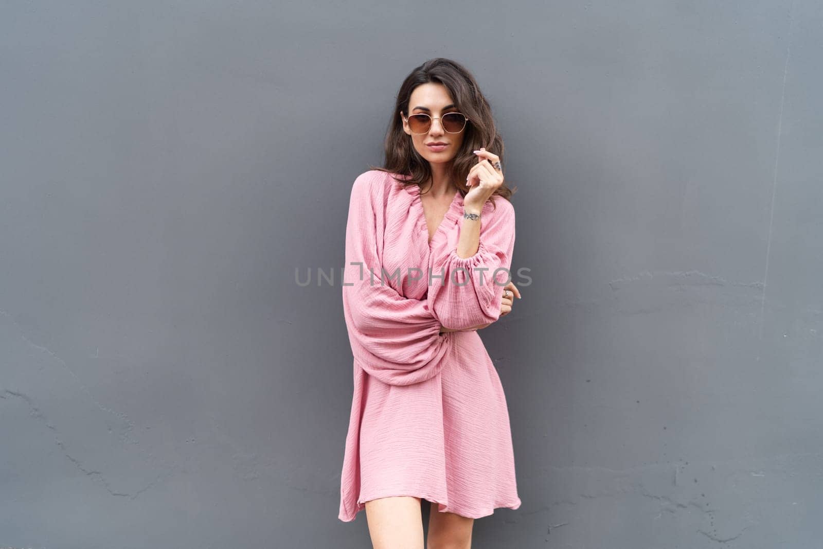 Young beautiful smiling cute romantic woman in trendy summer dress. Carefree woman posing in the street near grey wall. Positive model outdoors in sunglasses. Cheerful and happy.