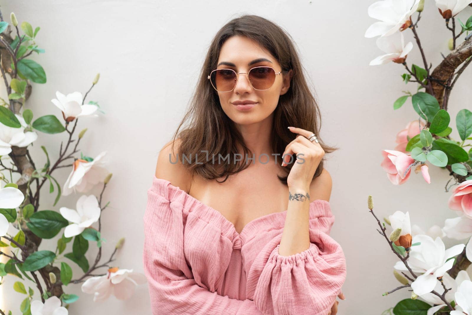 Young beautiful smiling cute romantic woman in trendy summer pink dress. Carefree woman posing in the street near white wall with flowers. Positive model outdoors in sunglasses. by kroshka_nastya