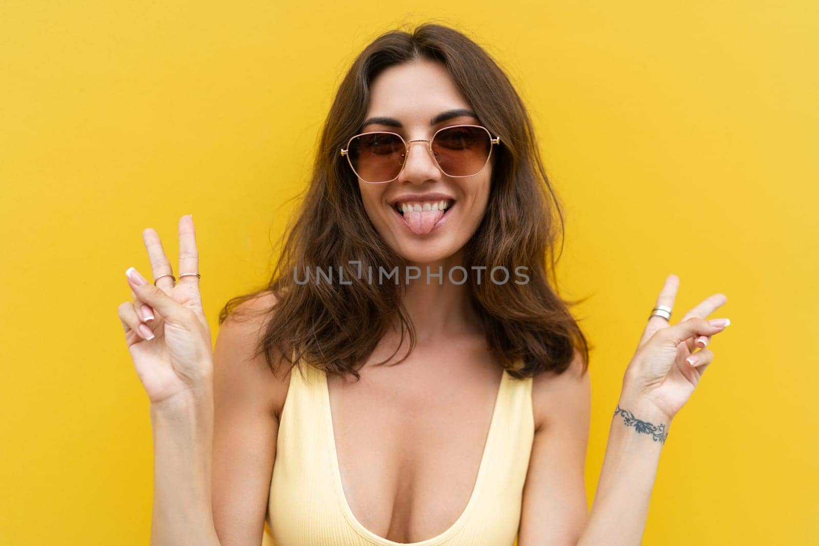 Young beautiful woman. Carefree woman posing in the street near yellow wall. Positive model outdoors in sunglasses. Happy and cheerful showing v sign by kroshka_nastya