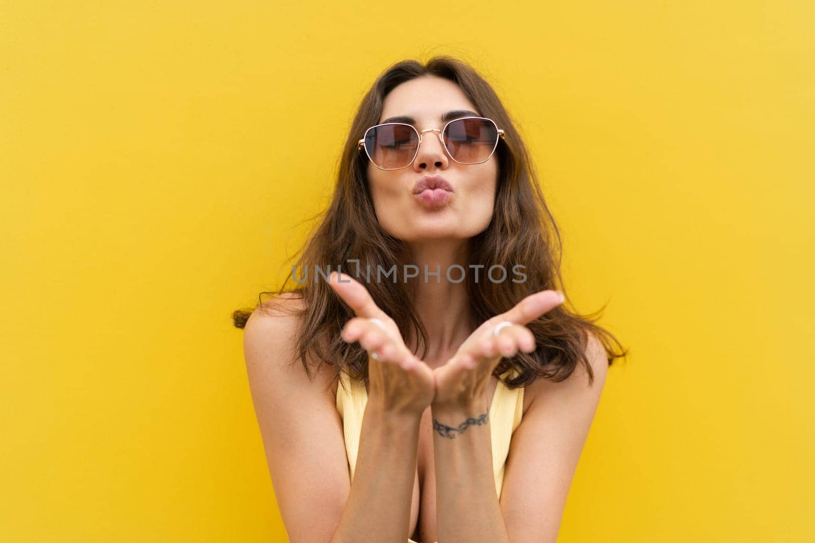 Young beautiful woman. Carefree woman posing in the street near yellow wall. Positive model outdoors in sunglasses. Happy and cheerful send a kiss