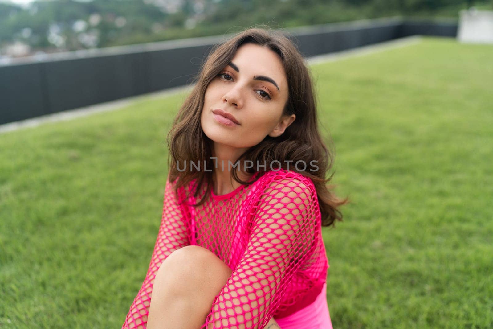 A slender young woman in a bright swimsuit on the grass by the pool. Slim athletic girl posing, tender romantic, looking at the camera