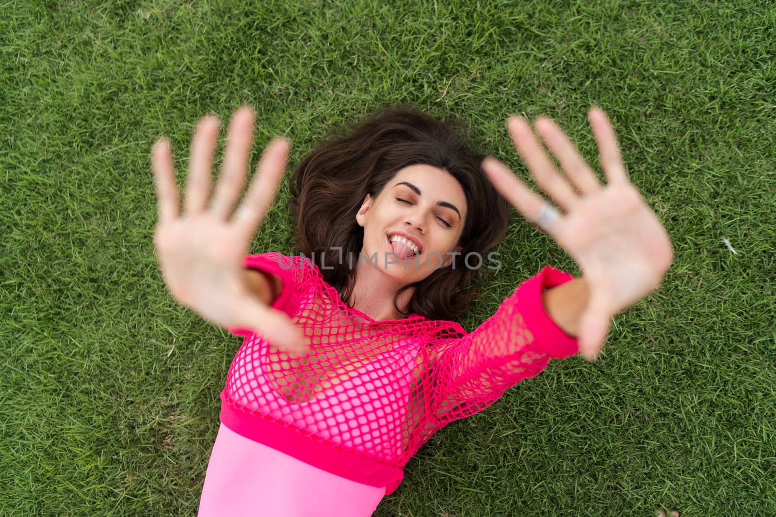 A slender young woman in a bright swimsuit on the grass by the pool. Slim athletic girl posing, tender romantic, looking at the camera