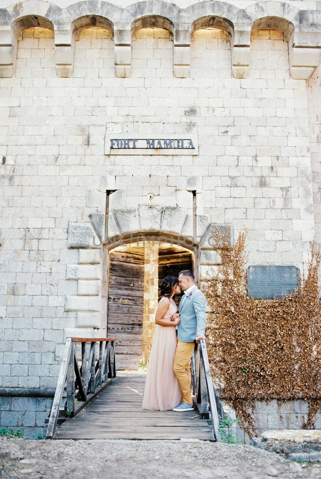 Bride and groom stand together holding hands on the bridge to Mamula Fort. High quality photo