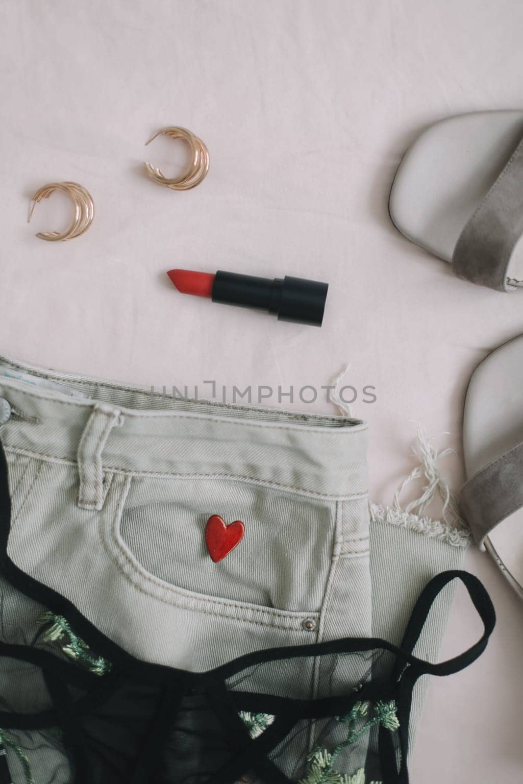 Overhead view of woman's casual spring outfit with phone or tablet, jeans, sandals, underwear, red lipstick and earrings on beige background, Flat lay, top view by paralisart