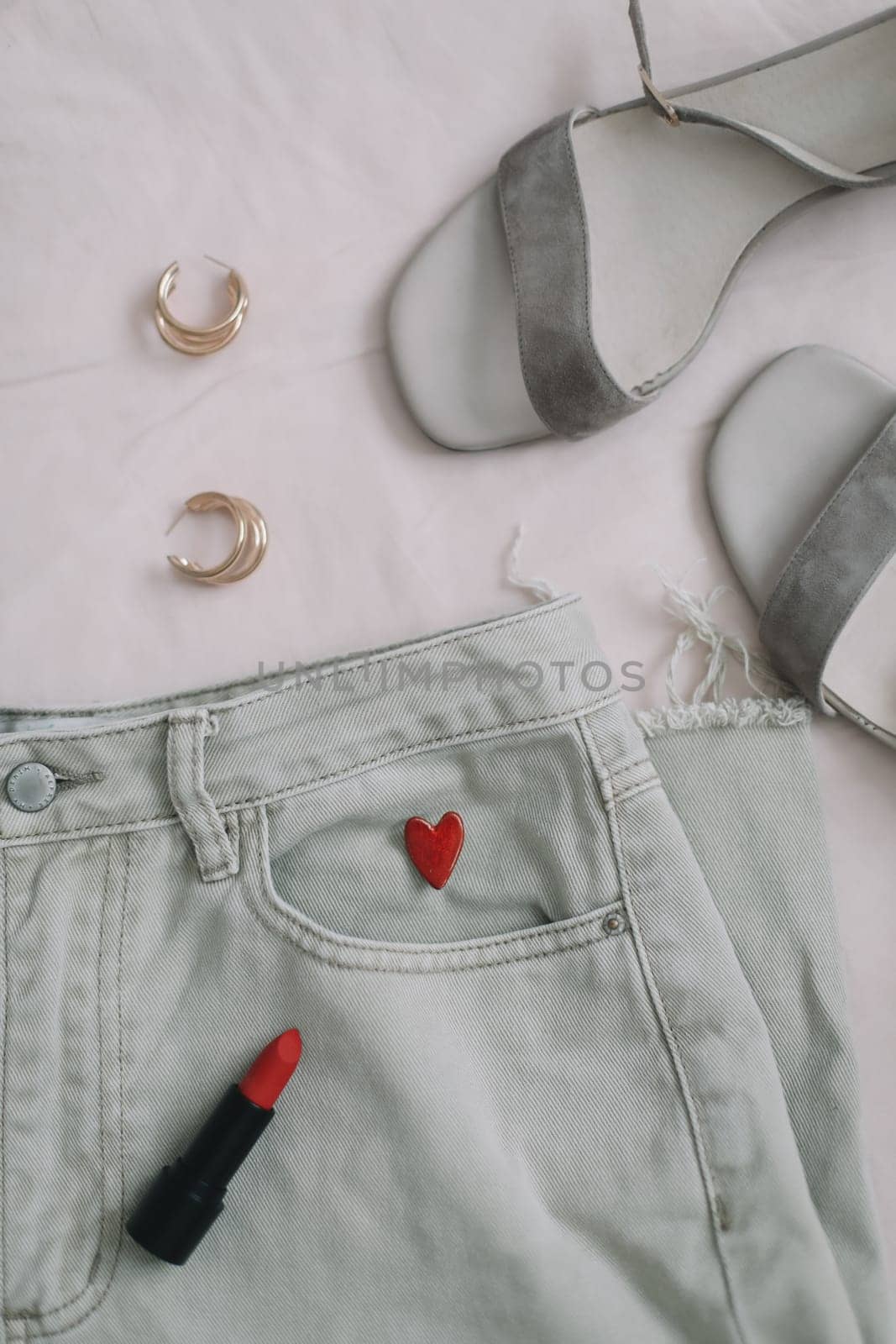Overhead view of woman's casual spring outfit with jeans, sandals, red lipstick and earrings on beige background, Flat lay, top view by paralisart