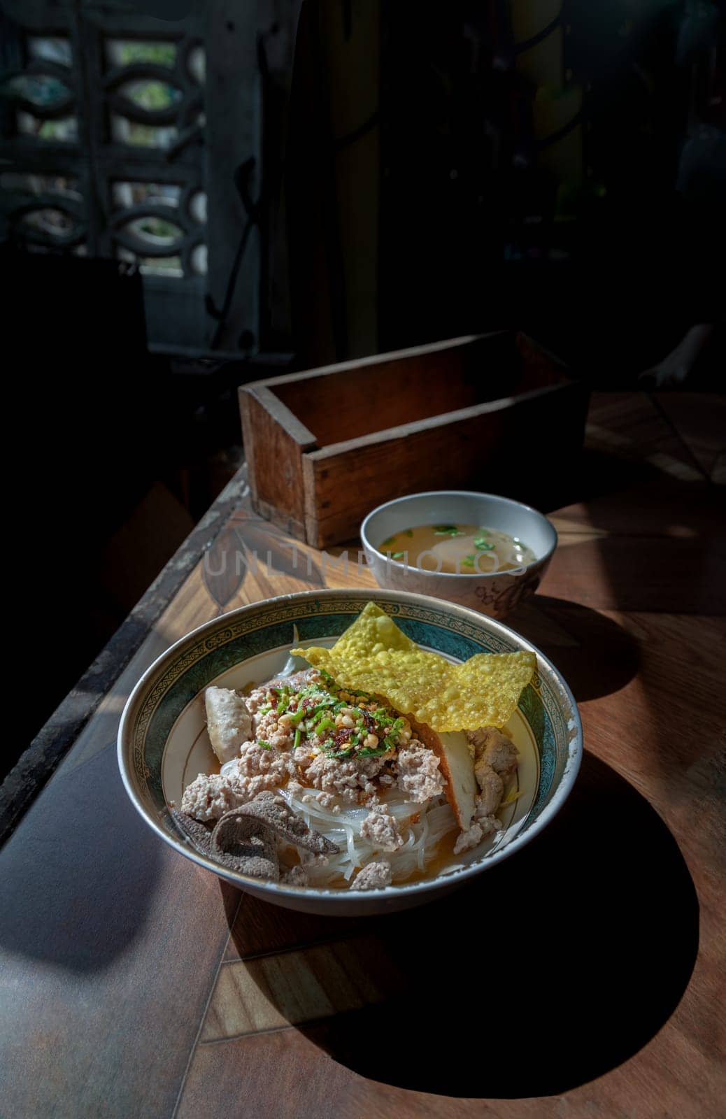 Steamed Thin rice noodles without soup with Meatball, Fish sticks, Minced pork, Boiled pork liver and Fried wonton topped with crackling and chopped dried chili in Bowl Served with soup. Traditional asian food style, Space for text, Selective Focus.