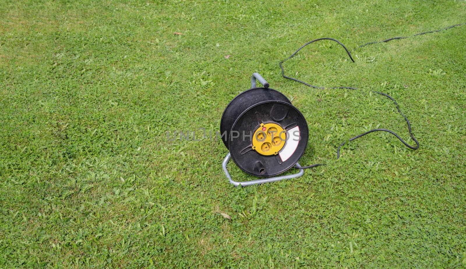 Black electric power cord and plug socket outlet on green grass field outdoor. High quality photo