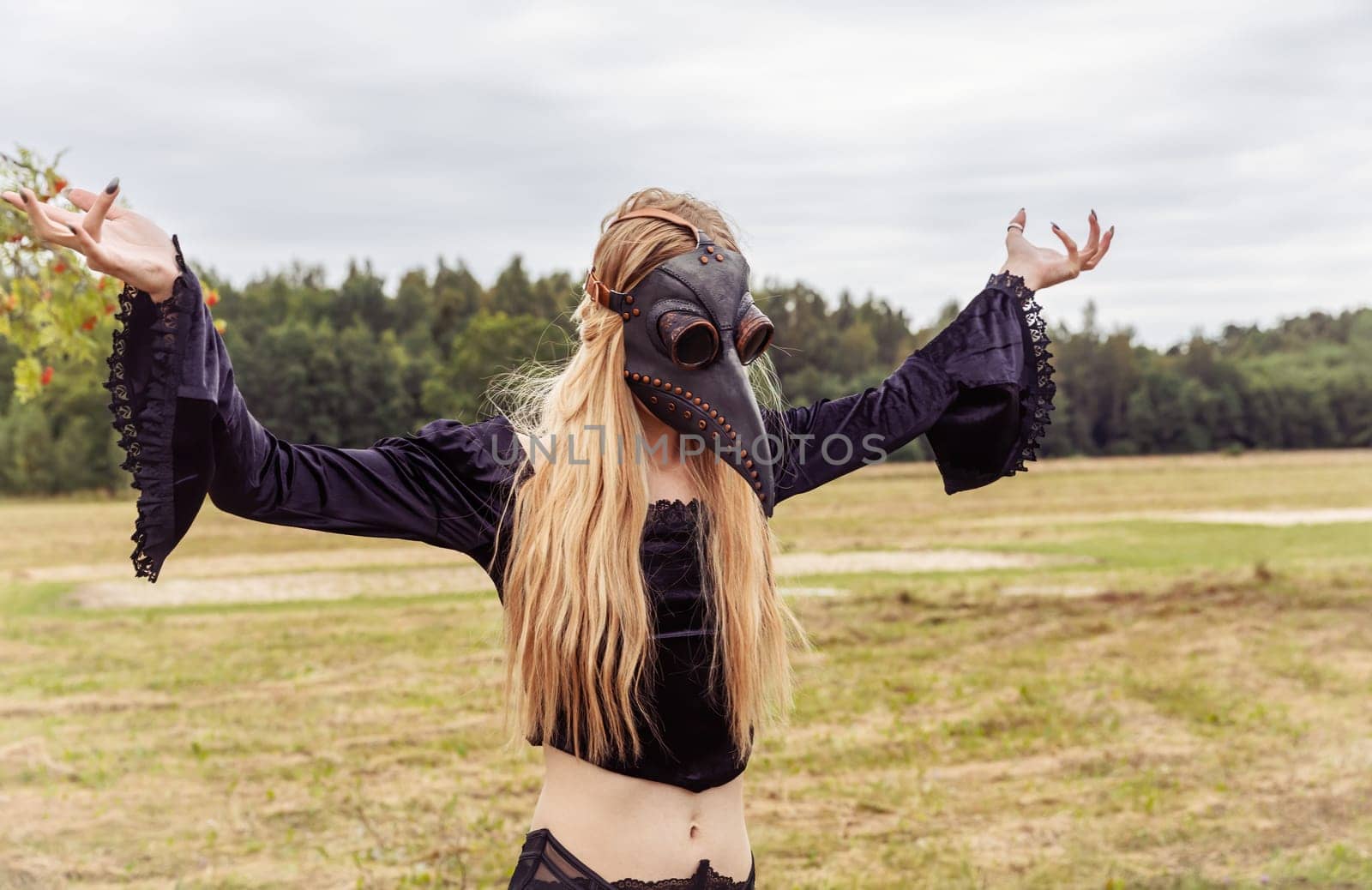 An eerie and surreal photo of a woman in a crow mask standing in a field.