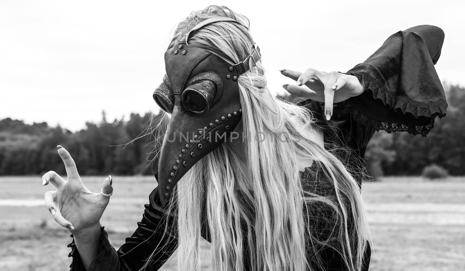 An eerie and surreal photo of a woman in a crow mask standing in a field. Black and white image