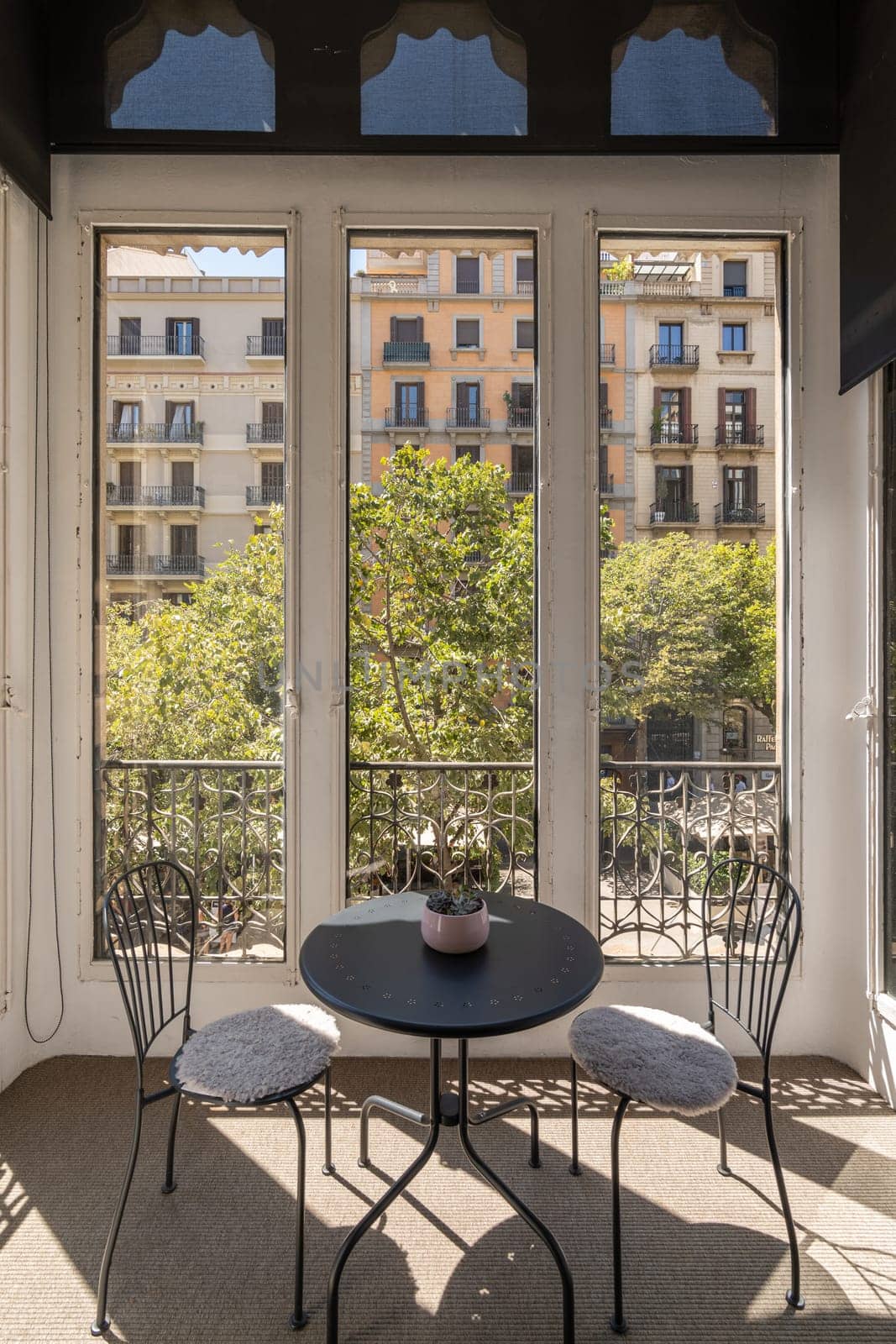 Two iron chairs and table on closed glazed terrace with beautiful view of cozy new area of warm country on sunny summer day. Concept of a romantic hotel room for honeymooners by apavlin