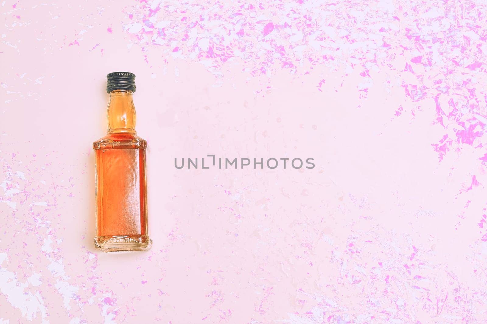 Small bottle alcohol brandy, whiskey, cognac on pink magenta flower background by jovani68