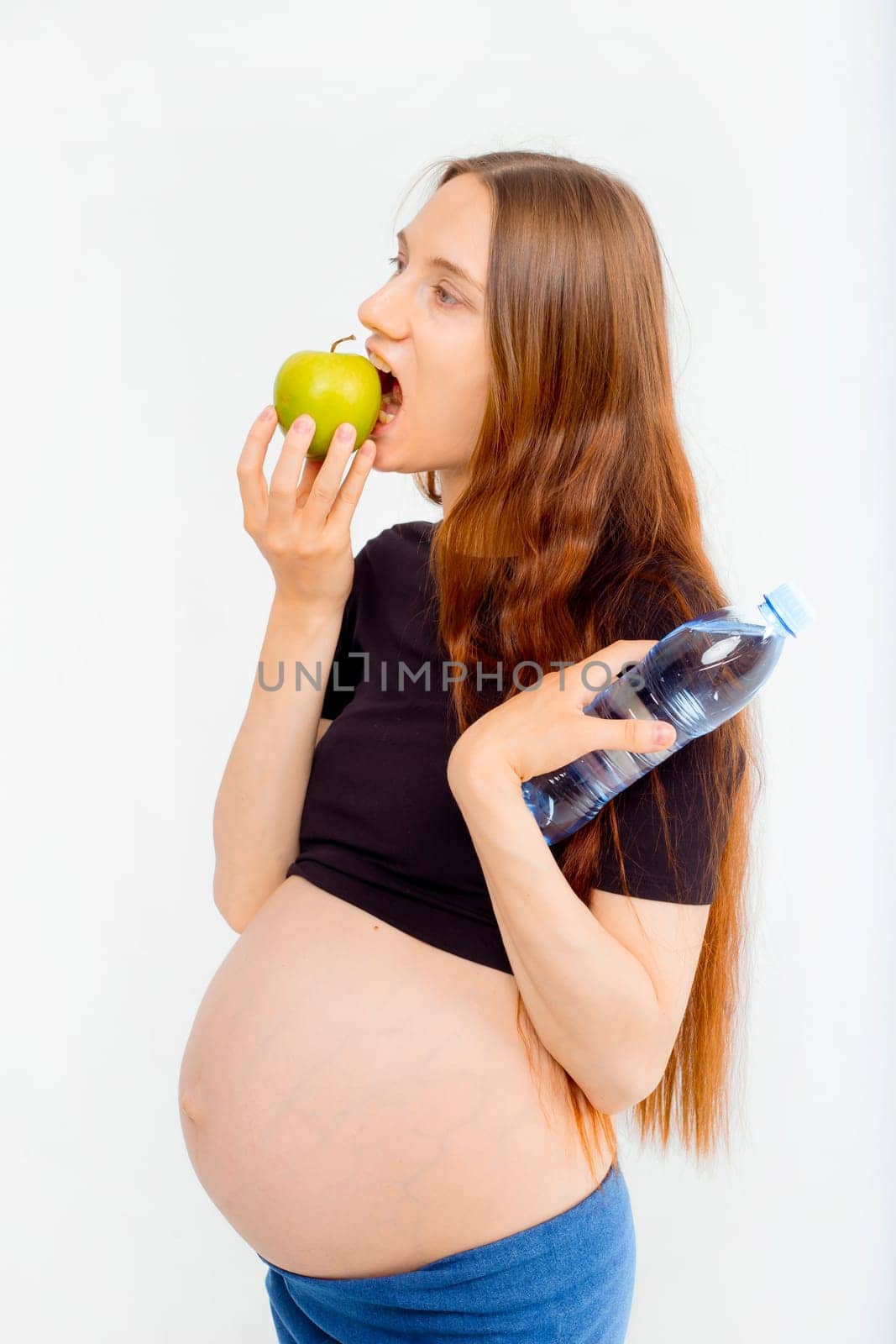 Pregnant woman propose apple for her belly copy space. Beautiful expectant lady having fresh snack, gray studio background. Healthy nutrition and pregnancy concept