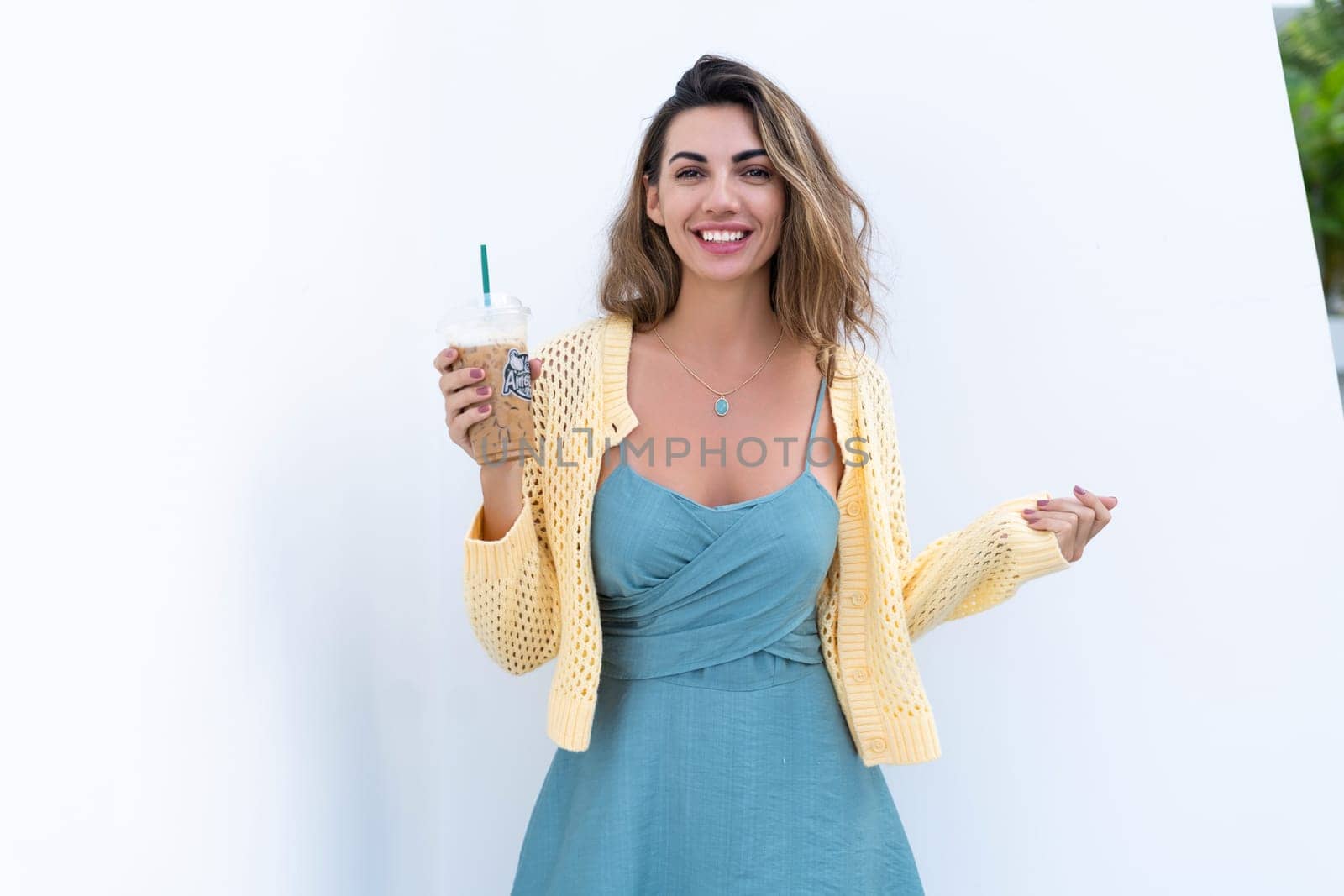 Portrait of beautiful woman in green summer dress on white background natural daylight, holding iced coffee cappuccino happy smiling excited