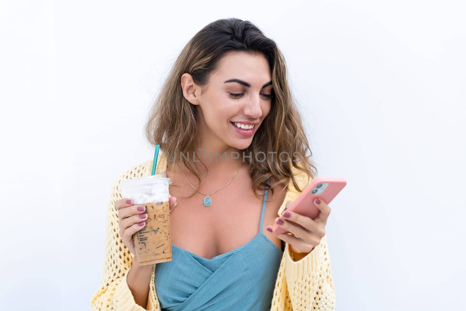 Portrait of beautiful woman in green summer dress on white background natural daylight, holding iced coffee cappuccino and phone thoughtful smiling