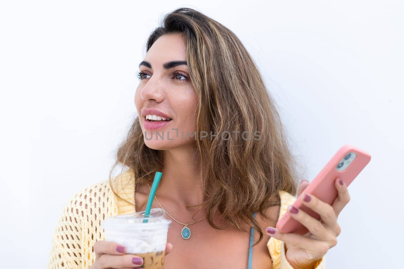 Portrait of beautiful woman in green summer dress on white background natural daylight, holding iced coffee cappuccino and phone thoughtful smiling