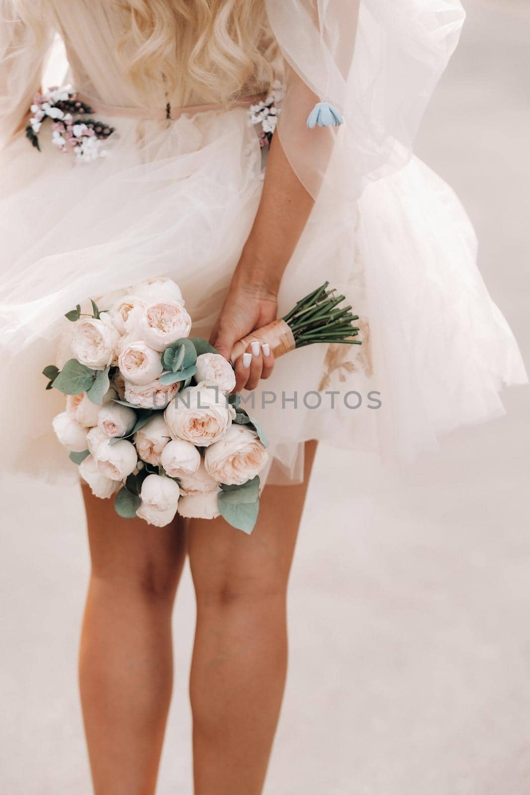 A bride with a short wedding dress holds a bouquet behind her back.