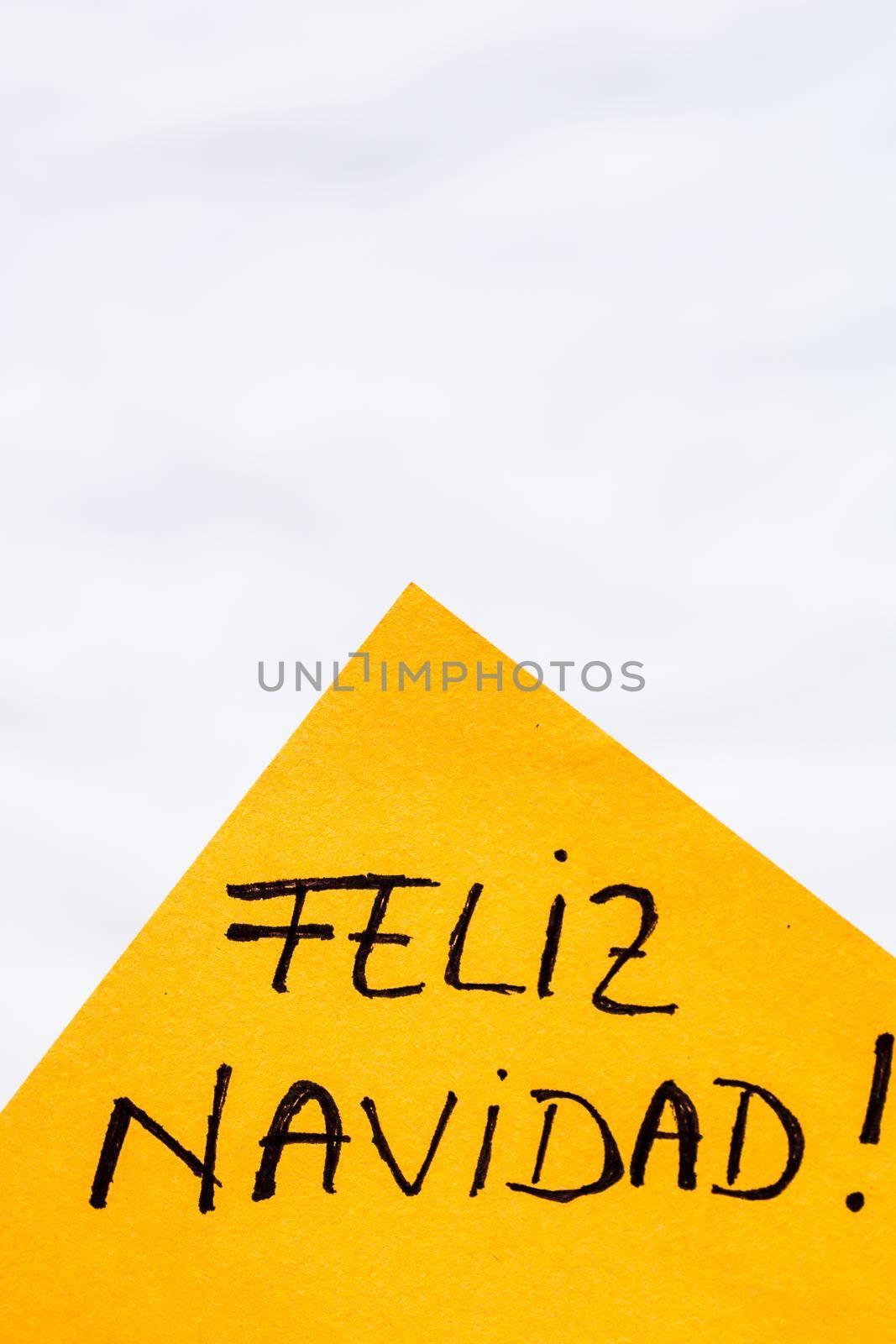 Feliz navidad (Merry Christmas) handwriting text close up isolated on orange paper with copy space. Writing text on memo post reminder. by vladispas