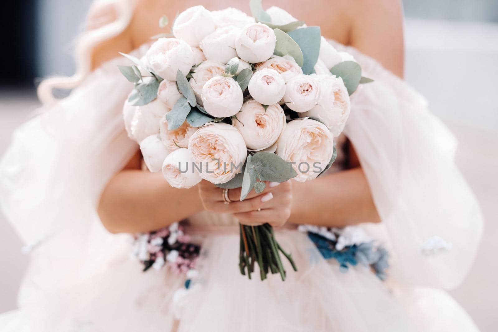 A bride in a wedding dress holds a bouquet of roses in her hands in front of her .close up.