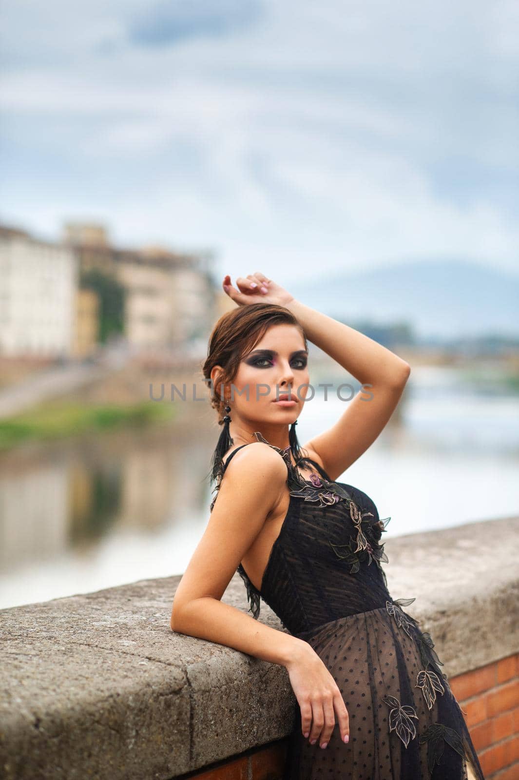 Beautiful stylish bride in a black dress stands on the embankment in Florence, Italy.