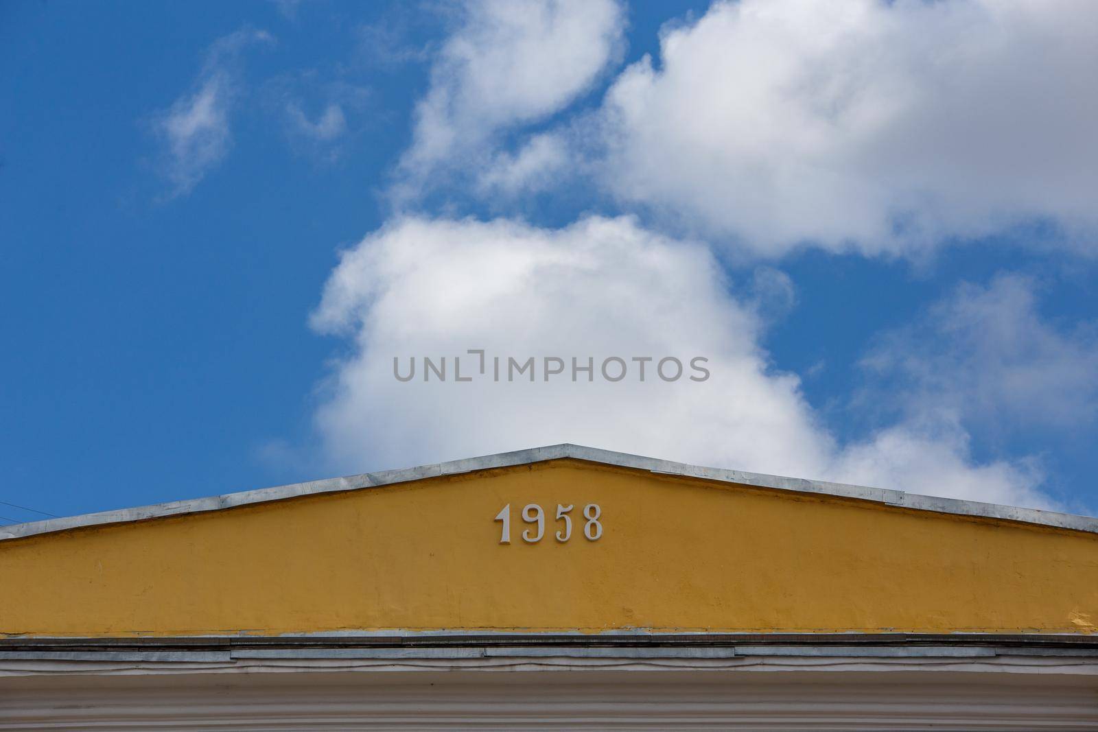 close-up view of yellow roof ridge wit digits 1958 on blue sky with white clouds background.