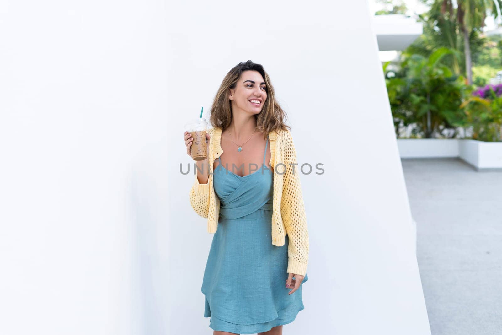 Portrait of beautiful woman in green summer dress on white background natural daylight, holding iced coffee cappuccino happy smiling excited