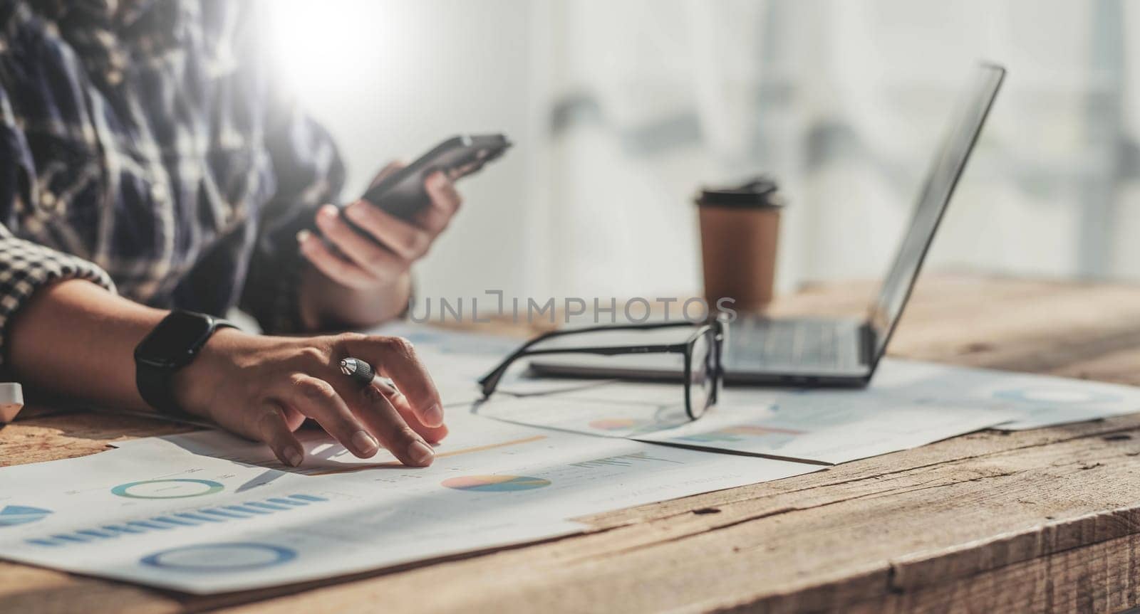 Young accountant hand holding smartphone to call marketing consultants and using laptop computer to analyze sales growth in the global workplace market. accounting concept..