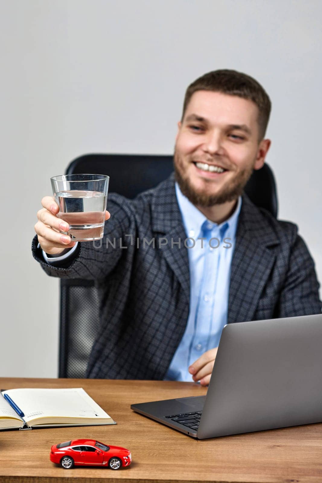 businessman in suit sitting by desk in front of laptop, holding glass of water. focus on glass