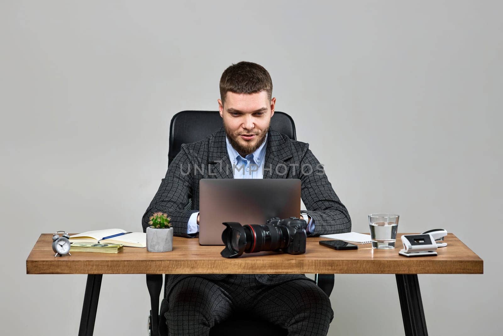 successful man photographer smiling cheerfully while working on laptop computer at desk. dslr camera on table