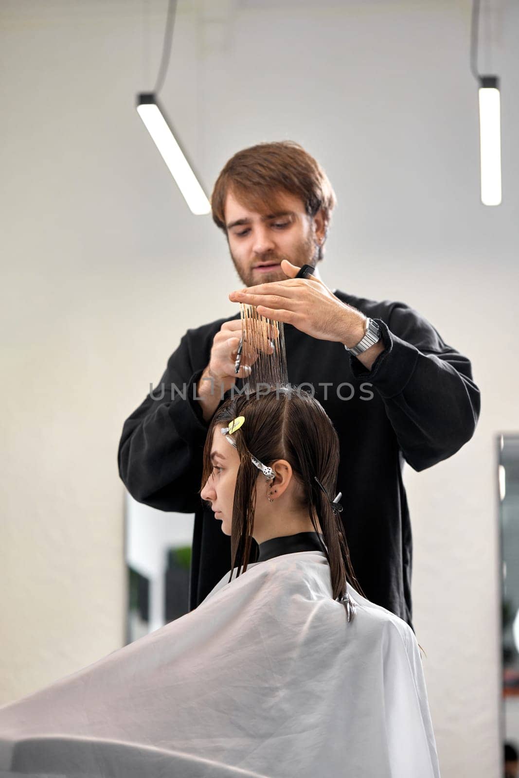 Professional male hairdresser with scissors cutting female hair in salon