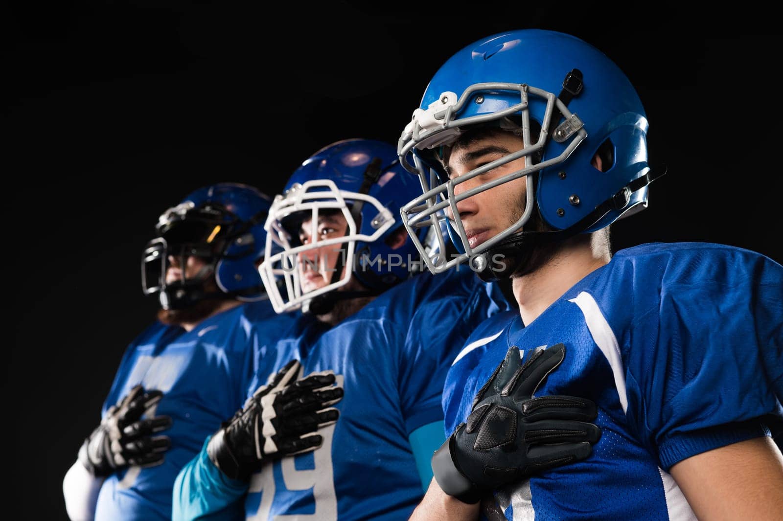 Portrait of three men in blue uniforms for American football with a hand on his chest on a black background. by mrwed54