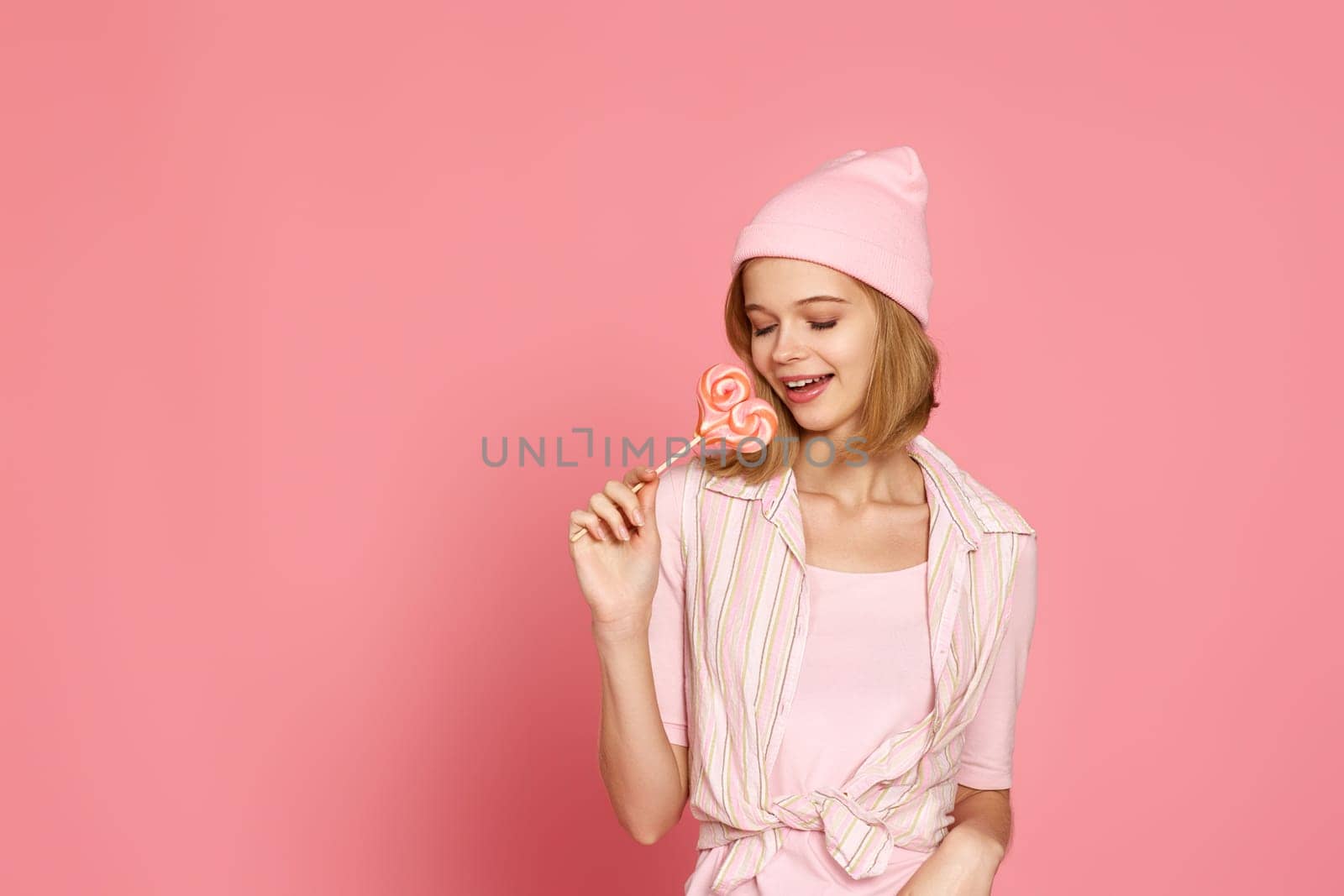 beautiful blonde woman holding lollipop on pink background. copy space