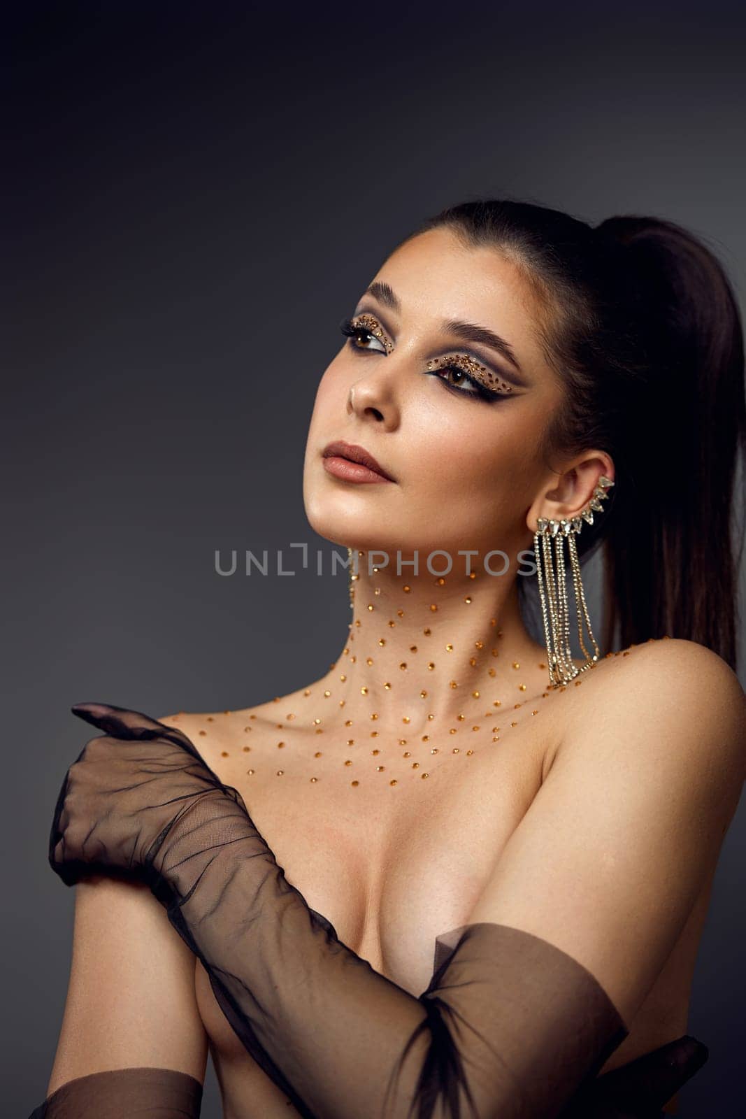 beauty fashionable model woman with creative eye makeup with arrows and rhinestones in long earring on gray background