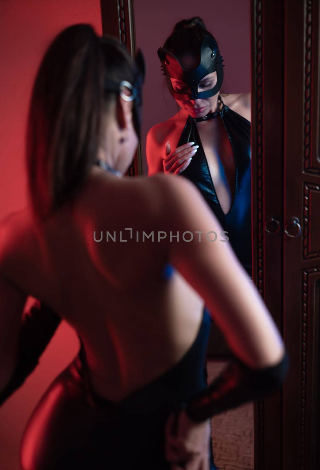 the Sexy girl in latex bdsm costume and cat mask in neon light in front of mirror