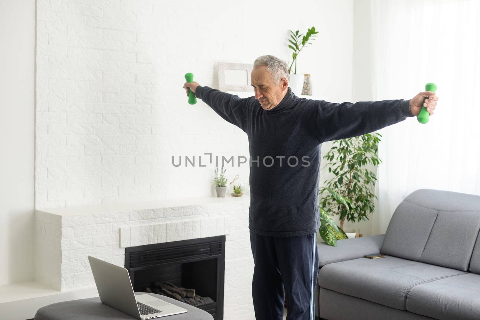 Sport in mature age. Happy middle-aged man doing stretching exercises in front of laptop at home, watching online tutorials, in living room interior by Andelov13