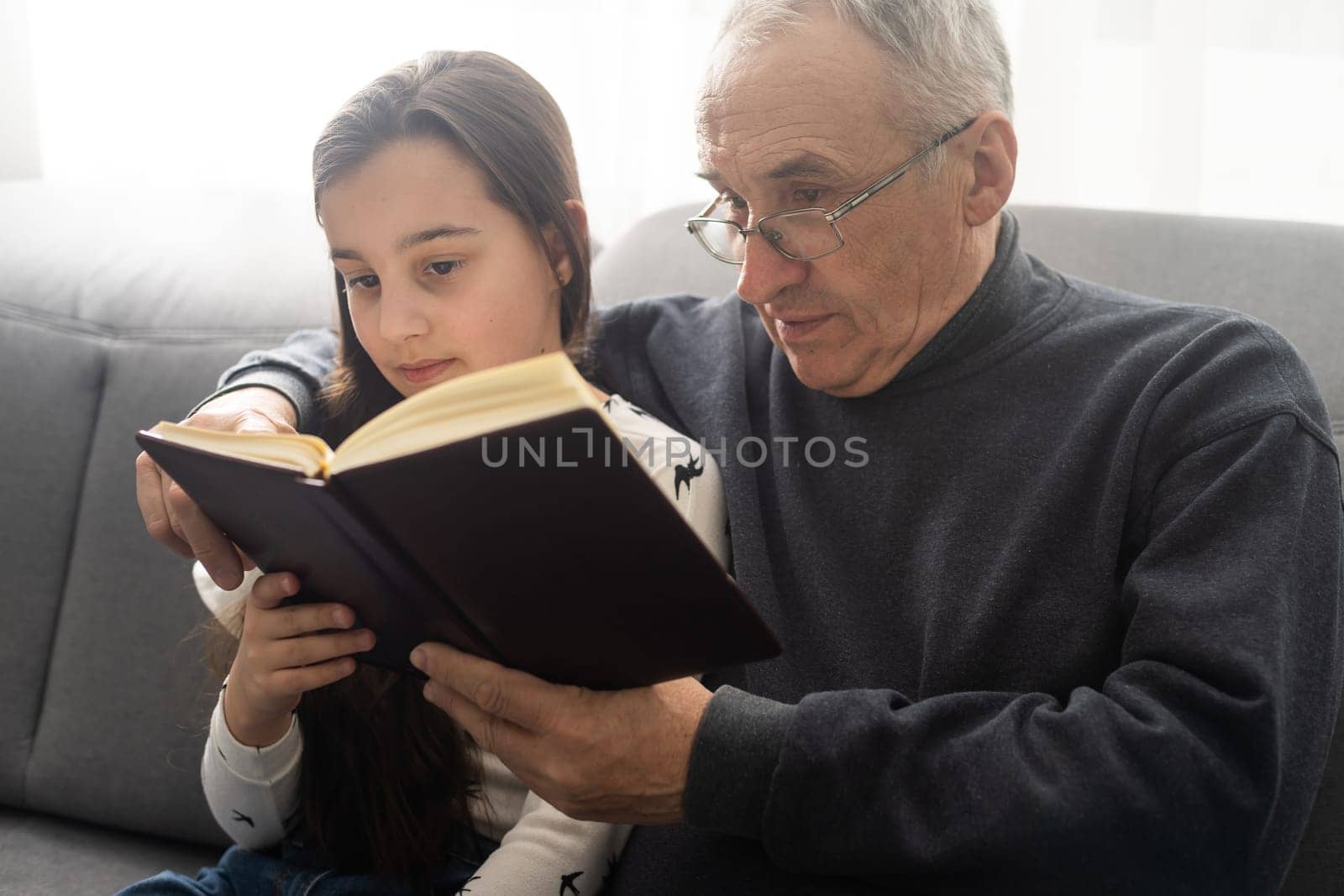 Book, family and children with a girl reading to her grandfather on the floor of their living at home. Kids, read and story with a senior man and granddaughter bonding in their house during a visit. by Andelov13