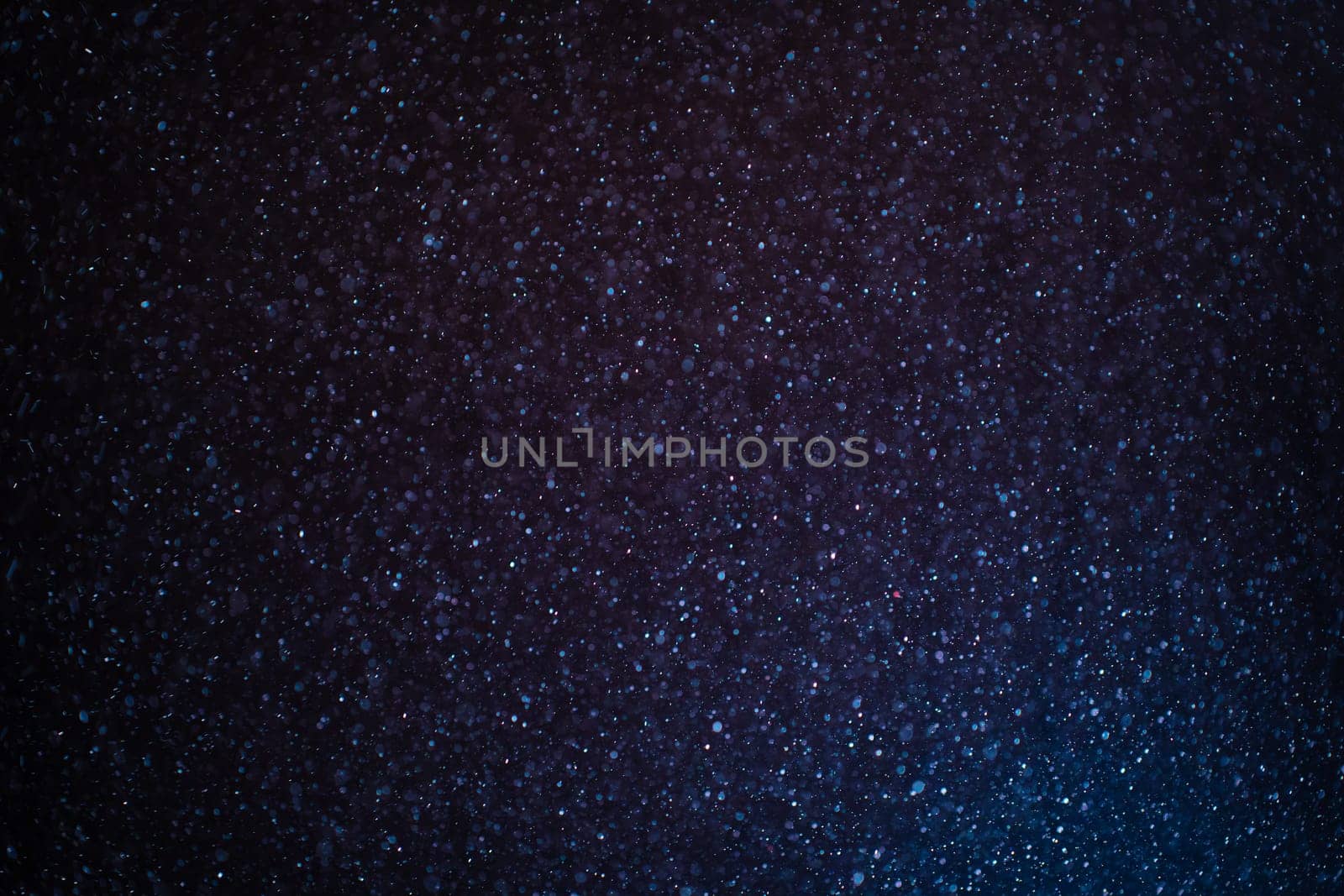Organic dust particles floating on a colorful light beam on black background. Glittering sparkling flickering overlay. High quality photo
