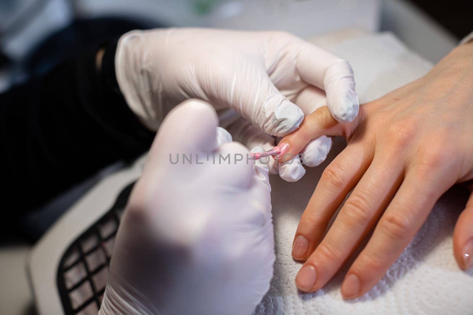 Latex gloves worn by a professional beautician. Top view of the client's and beautician's hands. A client of the beauty salon has a manicure performed.
