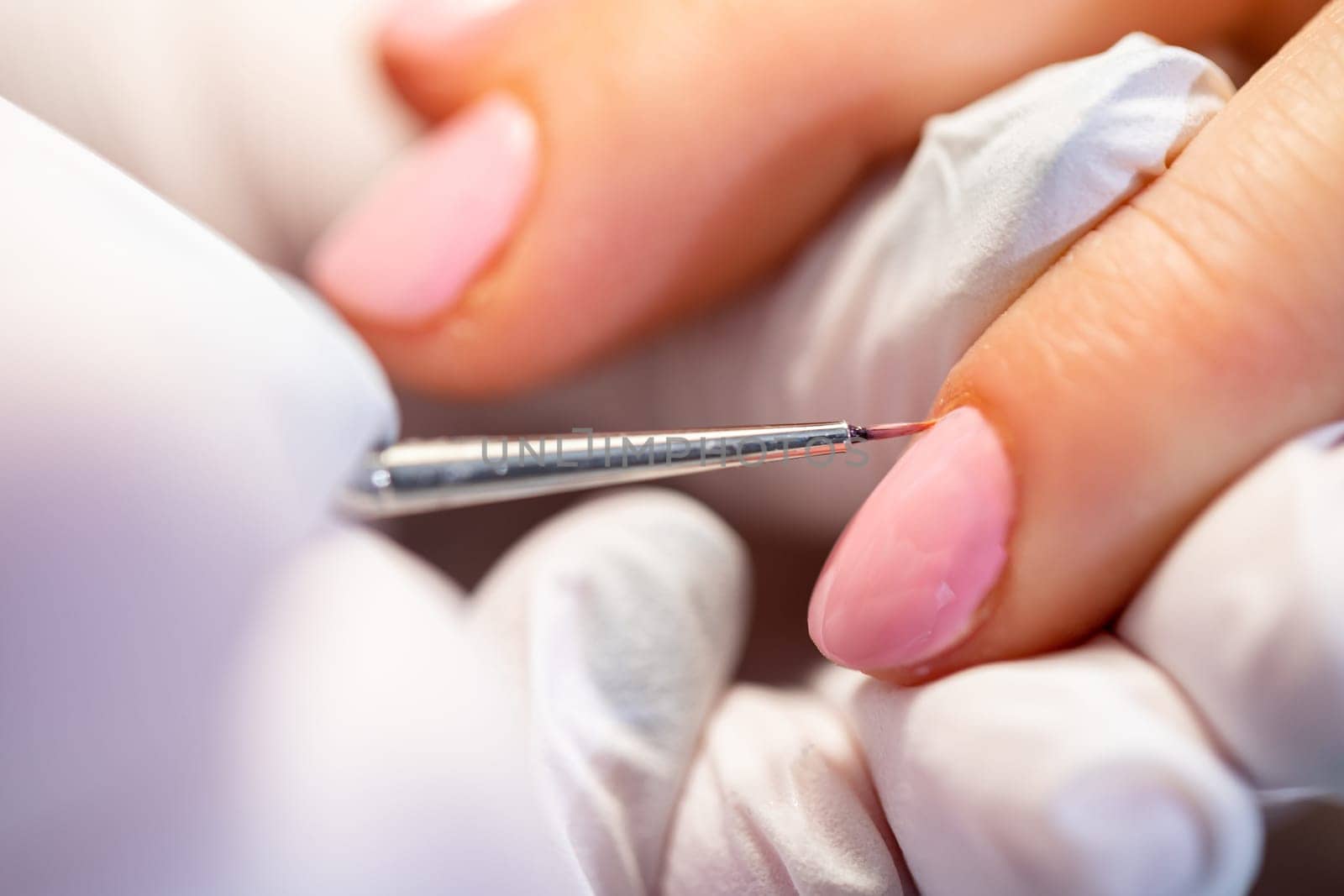 A large close-up of a woman's pink-painted nailsProfessional customer service. Precise nail painting in a beauty salon. Taking care of the nail plate.